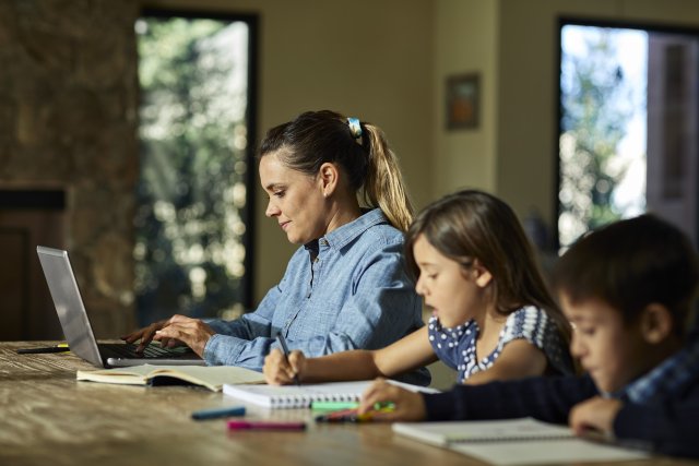 Madre e hijos sentados frente a su computadora y libros trabajando y estudiando