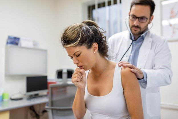 Mujer sentada en la camilla de la oficina del médico tosiendo frente al médico.