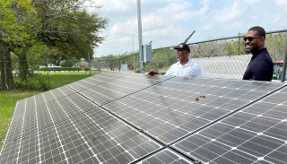 Administrador de la EPA y otro señor sonrientes parados al lado de unos paneles solares